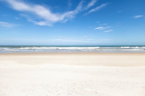 Uma extensa praia de areia com ondas suaves e céu azul límpido.