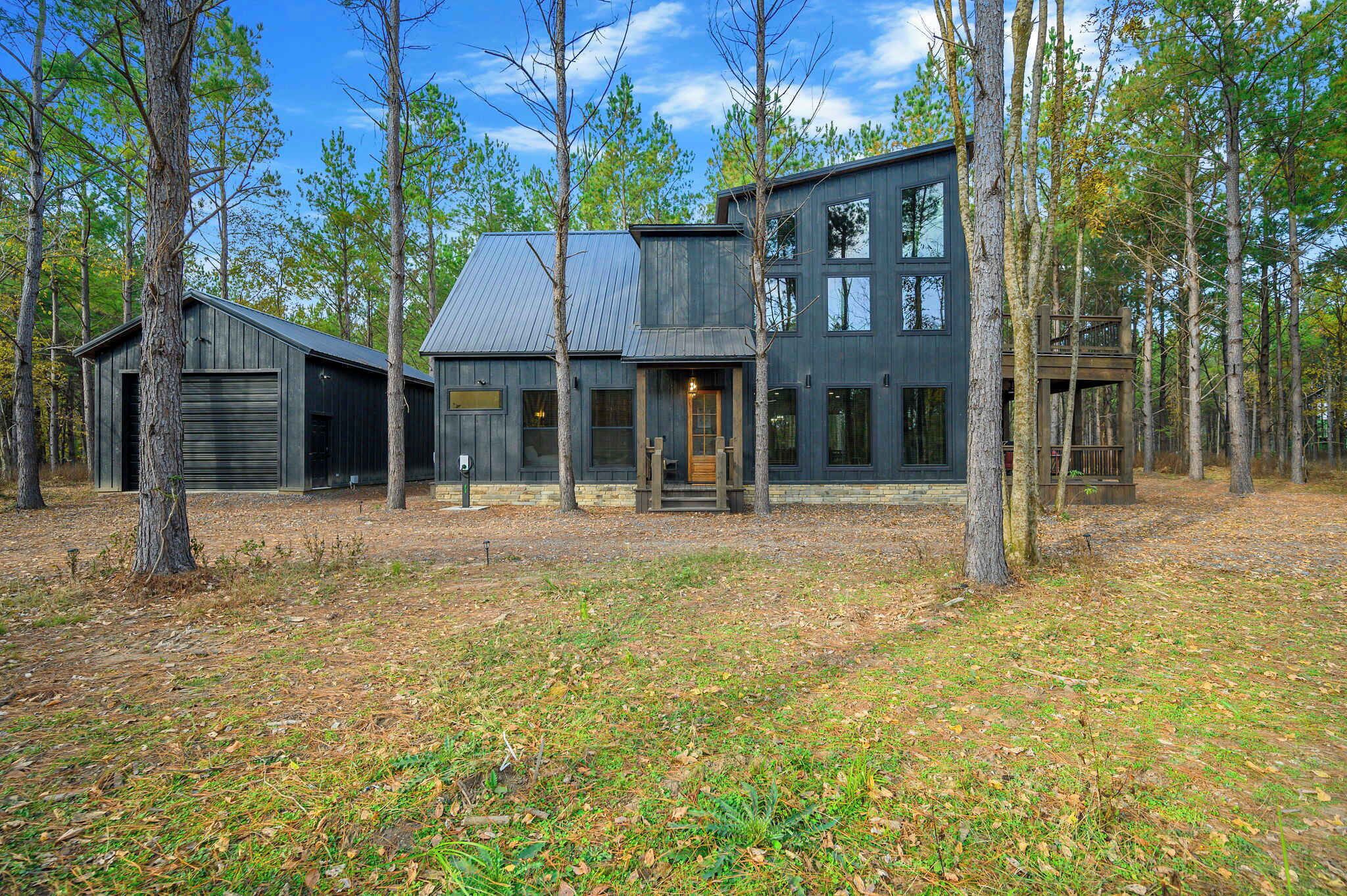 Une maison moderne à deux étages, entourée de grands arbres dans un espace boisé.