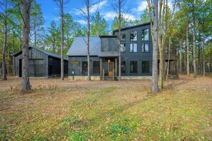 Uma casa moderna de dois andares rodeada por árvores altas numa área arborizada.