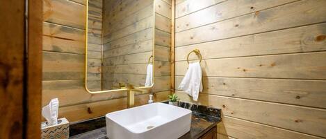 A wooden-paneled bathroom with a rectangular sink, a gold-framed mirror, and a towel hanging on the wall.