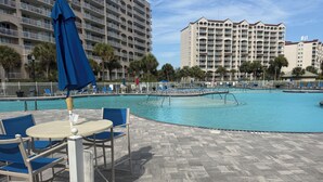 A poolside area with lounge chairs and a table, surrounded by tall buildings. - 1st Floor Golf View Condo, Free Beach Shuttle, pool/ Hot Tub, Barefoot Landing (North Myrtle Beach)