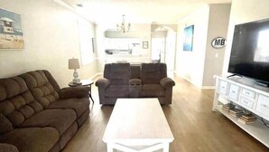 A living room with a ceiling fan, a sofa, a coffee table, and a TV stand. - 1st Floor Golf View Condo, Free Beach Shuttle, pool/ Hot Tub, Barefoot Landing (North Myrtle Beach)