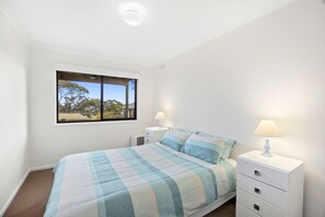 Ein Schlafzimmer mit einem Bett, zwei Nachttischen mit Lampen, einem Fenster und einer Deckenleuchte.