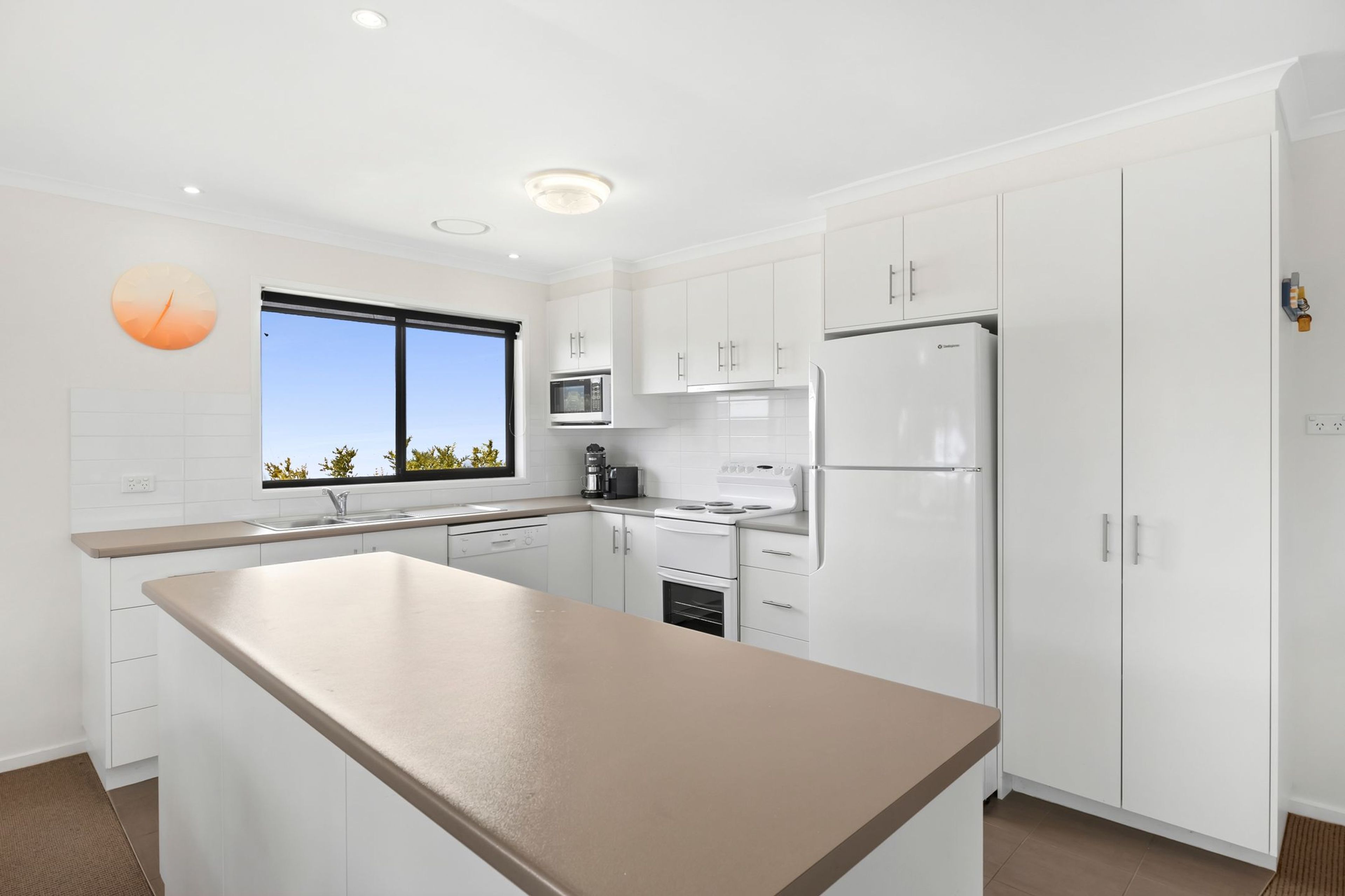 A modern kitchen with white cabinetry, a central island, a built-in oven, and a refrigerator.