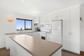 Eine moderne Küche mit weißen Schränken, einer zentralen Kochinsel, einem Einbauofen und einem Kühlschrank.