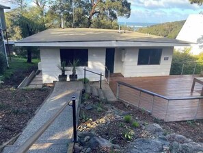 A modern house with a wooden deck, a concrete pathway leading to the entrance, and a small garden area. - Treetop Delight (Lorne)