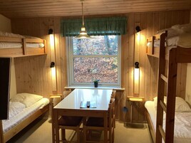 Una cabaña con literas, una mesa de comedor y un ventanal con vistas a árboles.