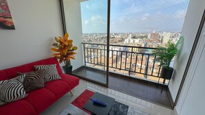 Ein modernes Wohnzimmer mit einem roten Sofa, einem kleinen Tisch und einem Balkon mit Blick auf die Stadt.