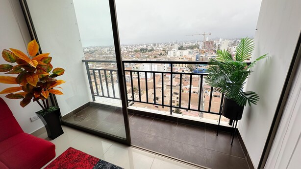 Ein Balkon mit Blick auf eine Stadtlandschaft, ein roter Stuhl und zwei Kübelpflanzen.