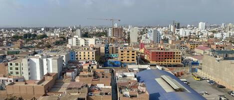 Un paisaje urbano con una combinación de edificios residenciales y comerciales, una estructura con techo azul destacada, y una grúa de construcción a lo lejos.