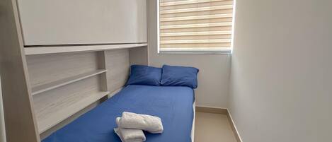 Une petite pièce, bien rangée, avec un lit, une fenêtre équipée de stores et une armoire intégrée.