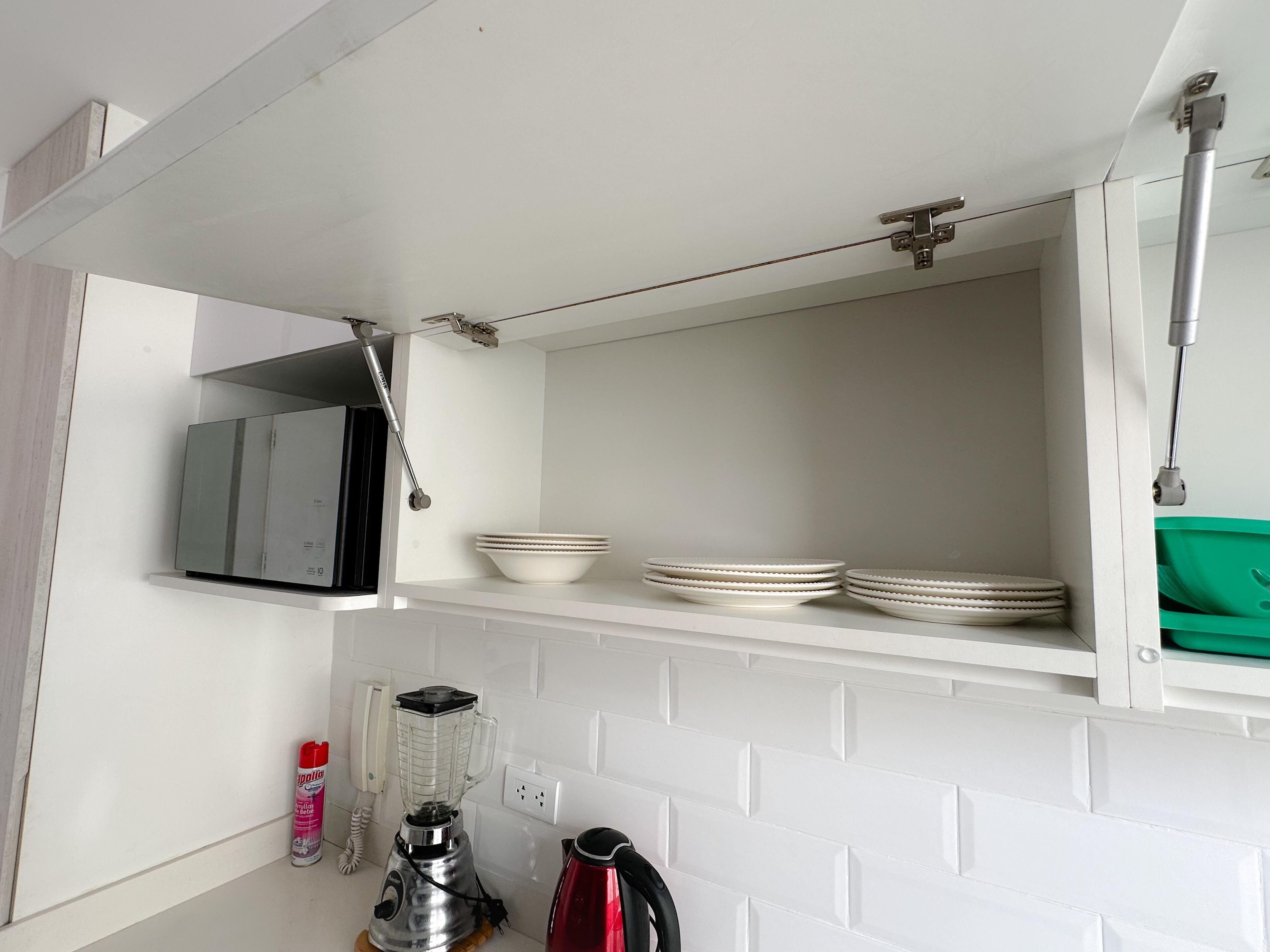 A kitchen with white cabinets, a blender, a kettle, and a green storage box.