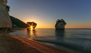 Un paisaje costero con atardecer, formaciones rocosas y agua tranquila.