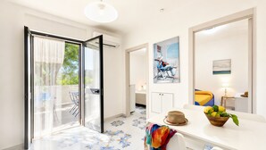 A modern room with a dining area, a painting of a person on a balcony, and a view of greenery outside. - Apartment 'Le Case Di Chri' with Wi-Fi and Air Conditioning (Mattinata)