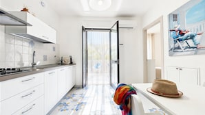 A modern kitchen with white cabinets, a tiled backsplash, and a view through an open door. - Apartment 'Le Case Di Chri' with Wi-Fi and Air Conditioning (Mattinata)