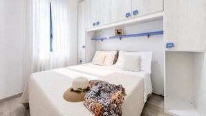 A bedroom with a bed, a wardrobe, a shelf with items, and a window with curtains. - Le Case Di Chri Apartment with Wi-Fi and Air Conditioning (Mattinata)