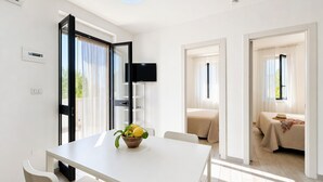 A modern hotel room with a white table, a flat-screen TV, a bed with a beige bedspread, and a view of the outdoors. - Le Case Di Chri Apartment with Wi-Fi and Air Conditioning (Mattinata)