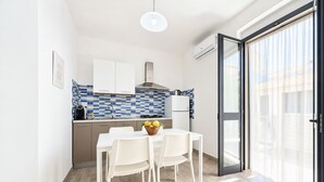 A modern kitchen with white cabinets, a tiled backsplash, and a dining area with a table and chairs. - Le Case Di Chri Apartment with Wi-Fi and Air Conditioning (Mattinata)