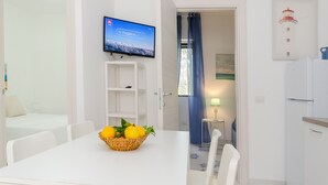 A modern hotel room with a dining table, a television, a kitchen area, and a view of a lighthouse. - Apartment 'Le Case Di Chri' with Wi-Fi and Air Conditioning (Mattinata)