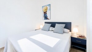 A bedroom with a bed, bedside tables, a nightstand, a lamp, and a painting on the wall. - Apartment 'Le Case Di Chri' with Wi-Fi and Air Conditioning (Mattinata)