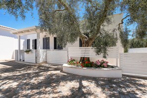 A white building with a covered porch, a tree, and a flower bed. - Apartment 'Le Case Di Chri' with Wi-Fi and Air Conditioning (Mattinata)