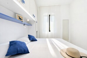 A hotel room with a bed, pillows, a hat, and a window with curtains. - Apartment 'Le Case Di Chri' with Wi-Fi and Air Conditioning (Mattinata)