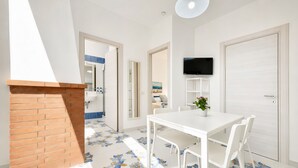 Una habitación moderna con una mesa blanca, sillas, televisor y chimenea.