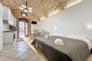 Un dormitorio con una colcha acolchada, un escritorio con silla, una kitchenette y vistas a la calle.
