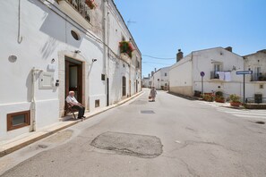 Una calle tranquila con edificios blancos, un hombre sentado en un banco y una mujer caminando.