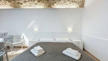 A modern hotel room with a bed, two bedside tables, a desk with chairs, and a ceiling with a unique texture.