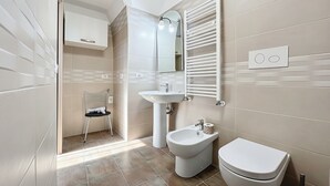 Een moderne badkamer met een wastafel op voetstuk, een toilet, een spiegel en een handdoekhouder.