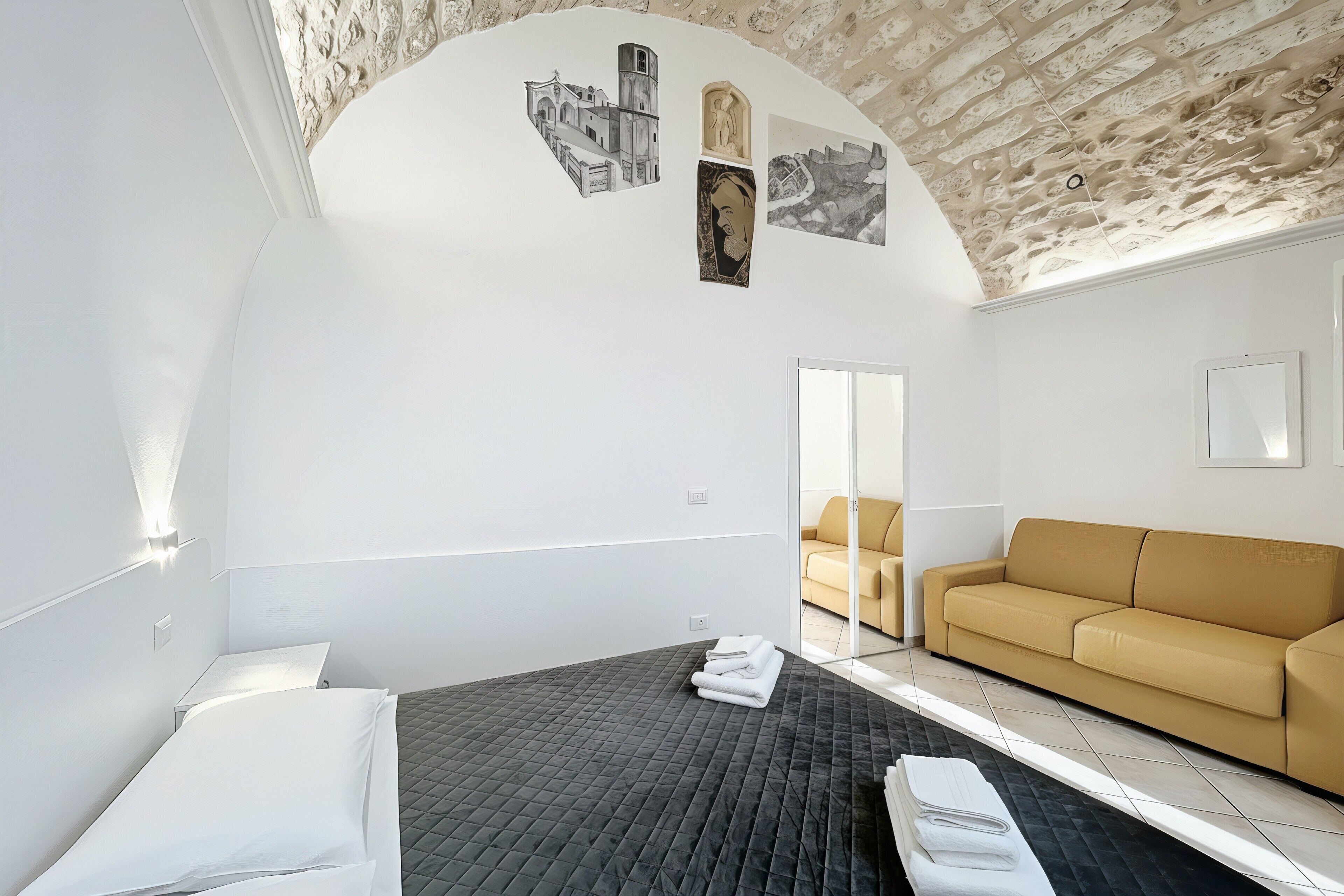 Ein modernes Hotelzimmer mit Bett, Sofa, einer Wand mit Kunstwerken und einer einzigartigen, strukturierten Decke.