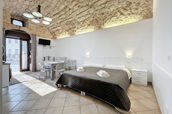 Un dormitorio con techo de piedra, una cama con cubrecama acolchado, una mesita de noche, una silla y una pequeña mesa con otra silla.
