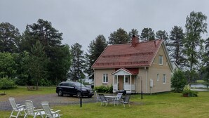Ett hus med ett rött tak, en veranda och en gräsmatta med utemöbler.