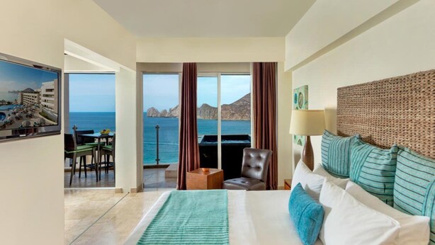 Una camera d'albergo con un grande letto, vista sul mare, zona pranzo e balcone.