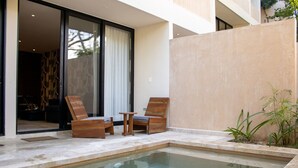 A swimming pool with two wooden lounge chairs and a small table, surrounded by a concrete deck and a beige wall. - Peregrina Tulum 102A 2BR Luxury Condo (Tulum)