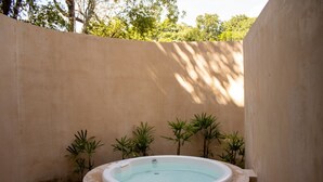 A spa area with a hot tub surrounded by plants and a concrete wall. - Peregrina Tulum 102A 2BR Luxury Condo (Tulum)