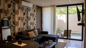 A modern living room with a dark sofa, a round coffee table, and a TV mounted on the wall. - Peregrina Tulum 102A 2BR Luxury Condo (Tulum)