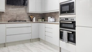 A modern kitchen with white cabinetry, a built-in microwave, a stove, and a large window above the sink. - 5 BR Flat |Spacious|Near Shepherd's Bush Stn.|ST (Greater London)