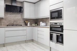 A modern kitchen with white cabinetry, a built-in microwave, a stove, and a large window above the sink. - 5 BR Flat |Spacious|Near Shepherd's Bush Stn.|ST (Greater London)
