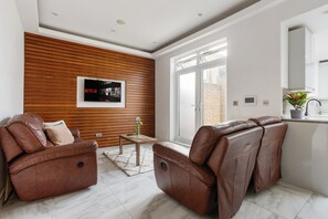 Un salon moderne avec des canapés en cuir, un mur d’accent en bois, un téléviseur et une grande fenêtre.