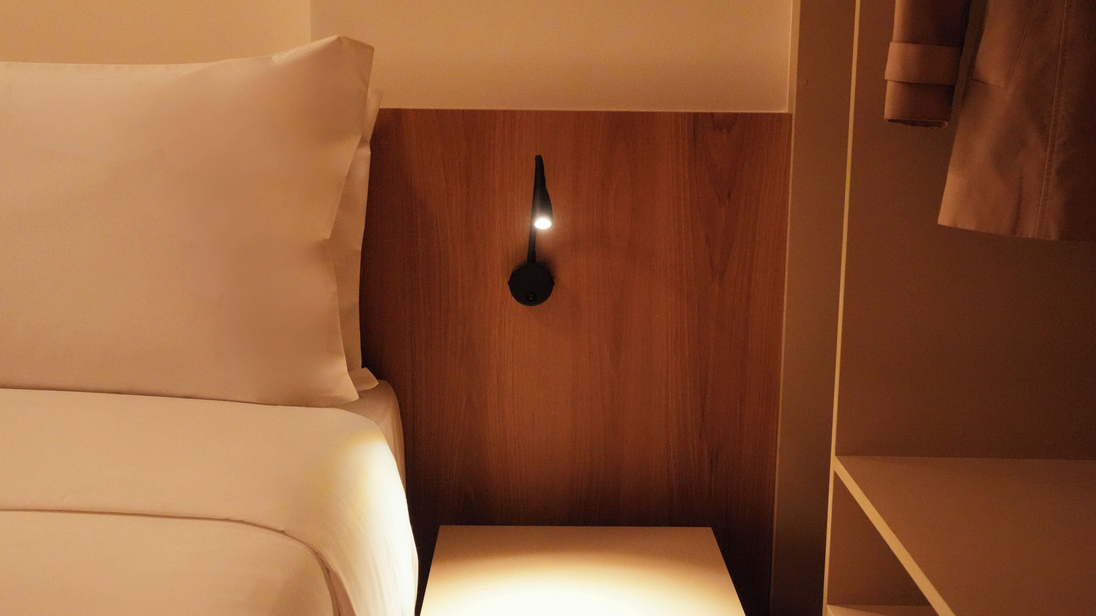 A hotel room with a bed, a bedside table, and a wall-mounted light fixture.