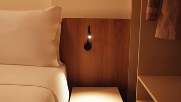 A hotel room with a bed, a bedside table, and a wall-mounted light fixture.