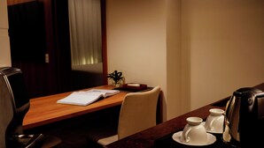 Habitació d'hotel amb un escriptori de fusta, una cadira, una cafetera i una petita planta.