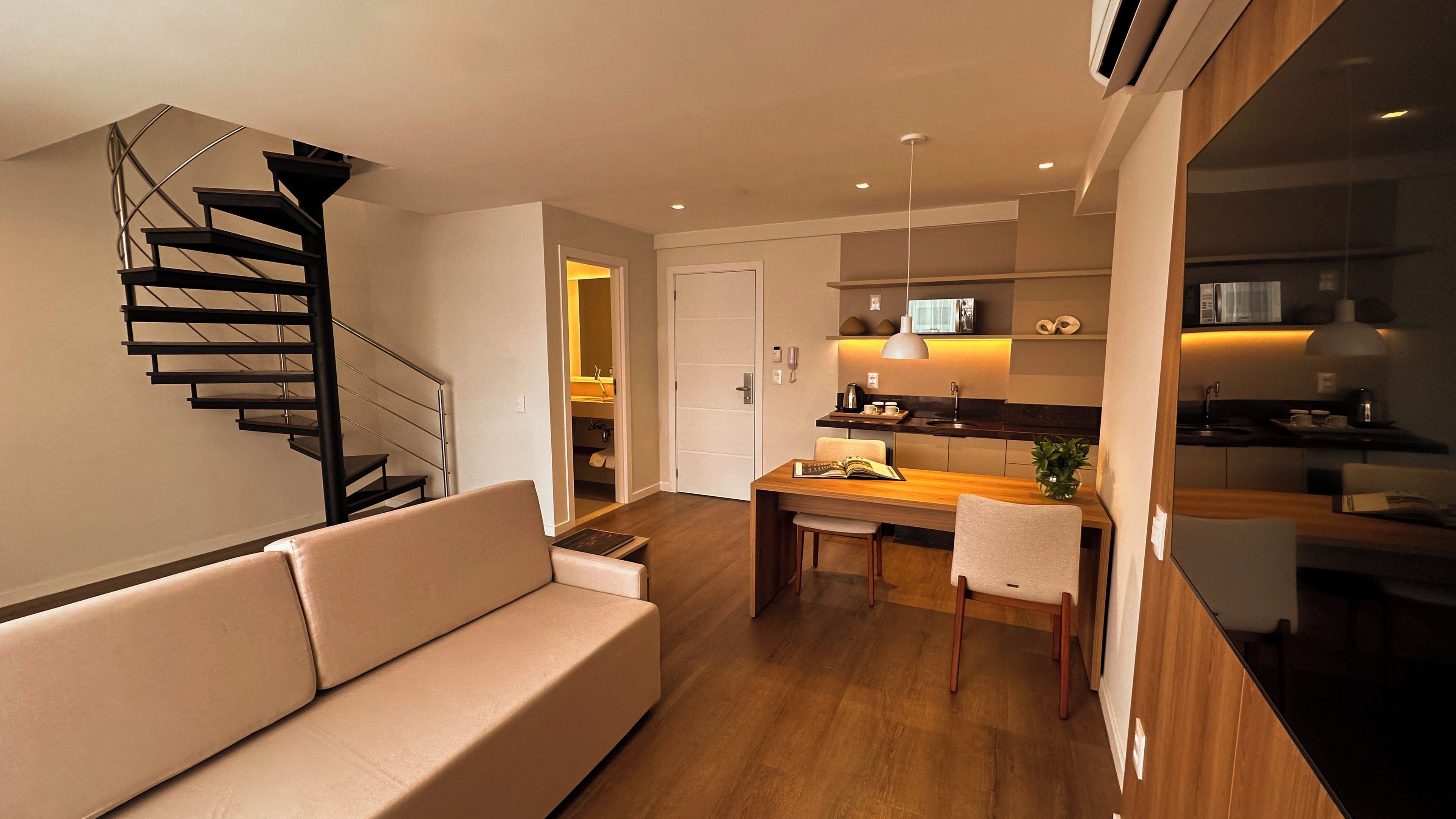 A modern living room with a staircase, a dining area, and a kitchen.