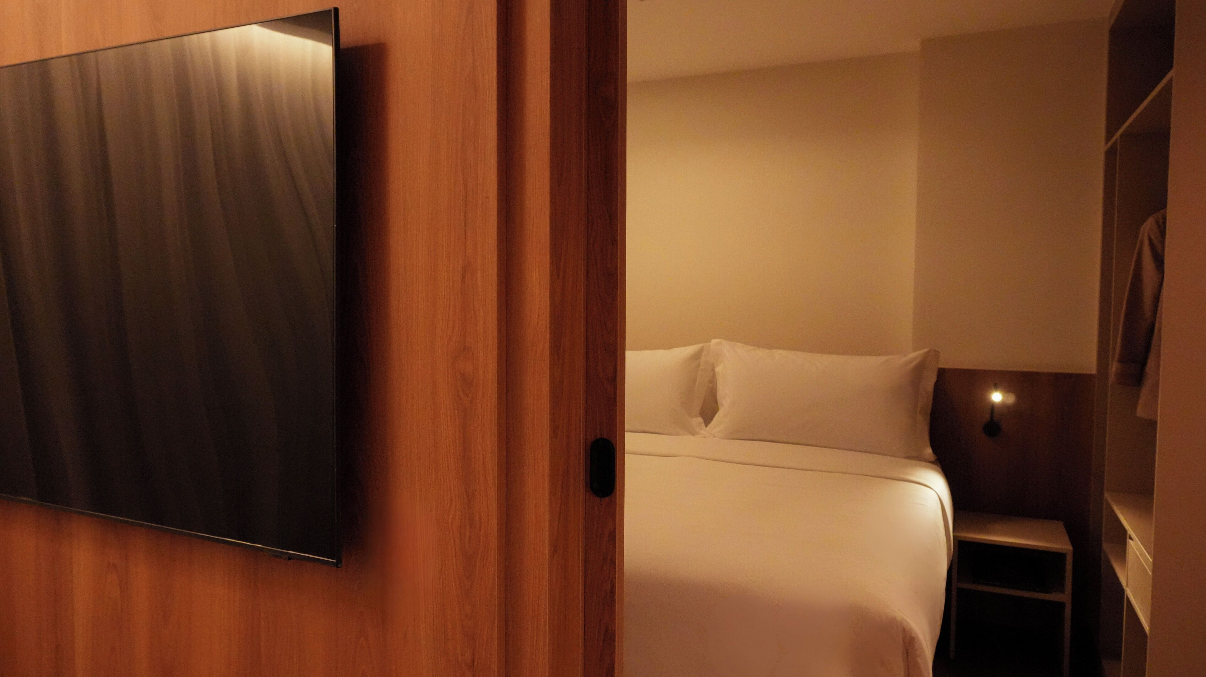 A hotel room with a bed, a TV mounted on the wall, and a small bedside table.