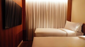 Habitación de hotel con dos camas, un televisor montado en la pared y un amplio ventanal con cortinas.