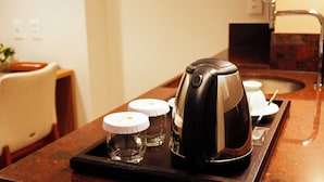 Una cafetera sobre una bandeja con tres tazas, un lavamanos y una silla en una habitación de hotel.