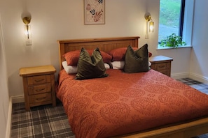 A bedroom with a wooden bed, red patterned bedding, two bedside tables, a nightstand, and a window with a view of greenery. - 3 Bed House - Sea Views, Balcony, Parking, Pets (Dunoon)
