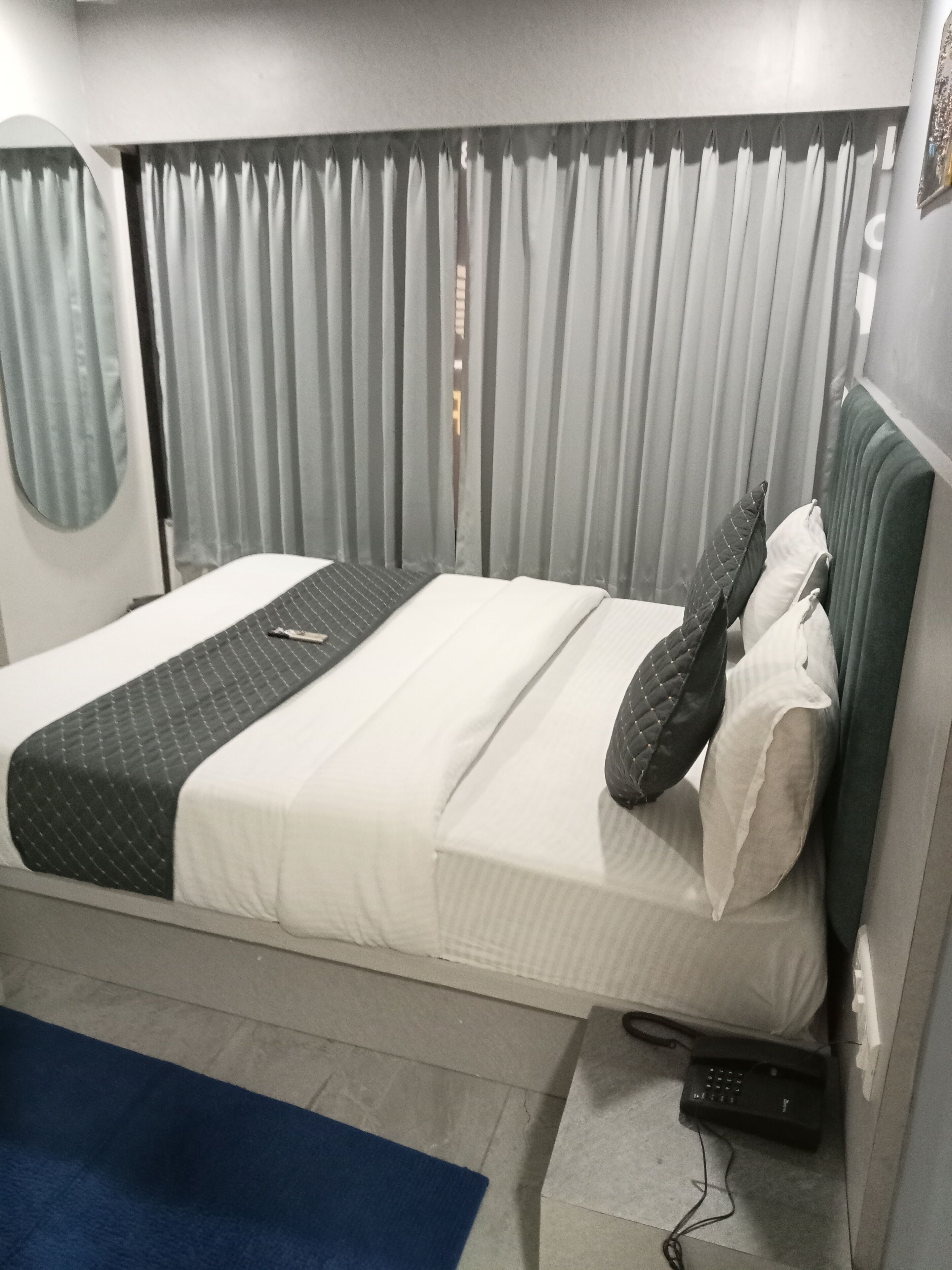 A single bed with a quilted blanket, pillows, and a remote control on the floor.